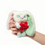 A hand holds a white Plushie Dreadfuls bunny with green ears and a red Cancer Plush Keychain crab on white background.