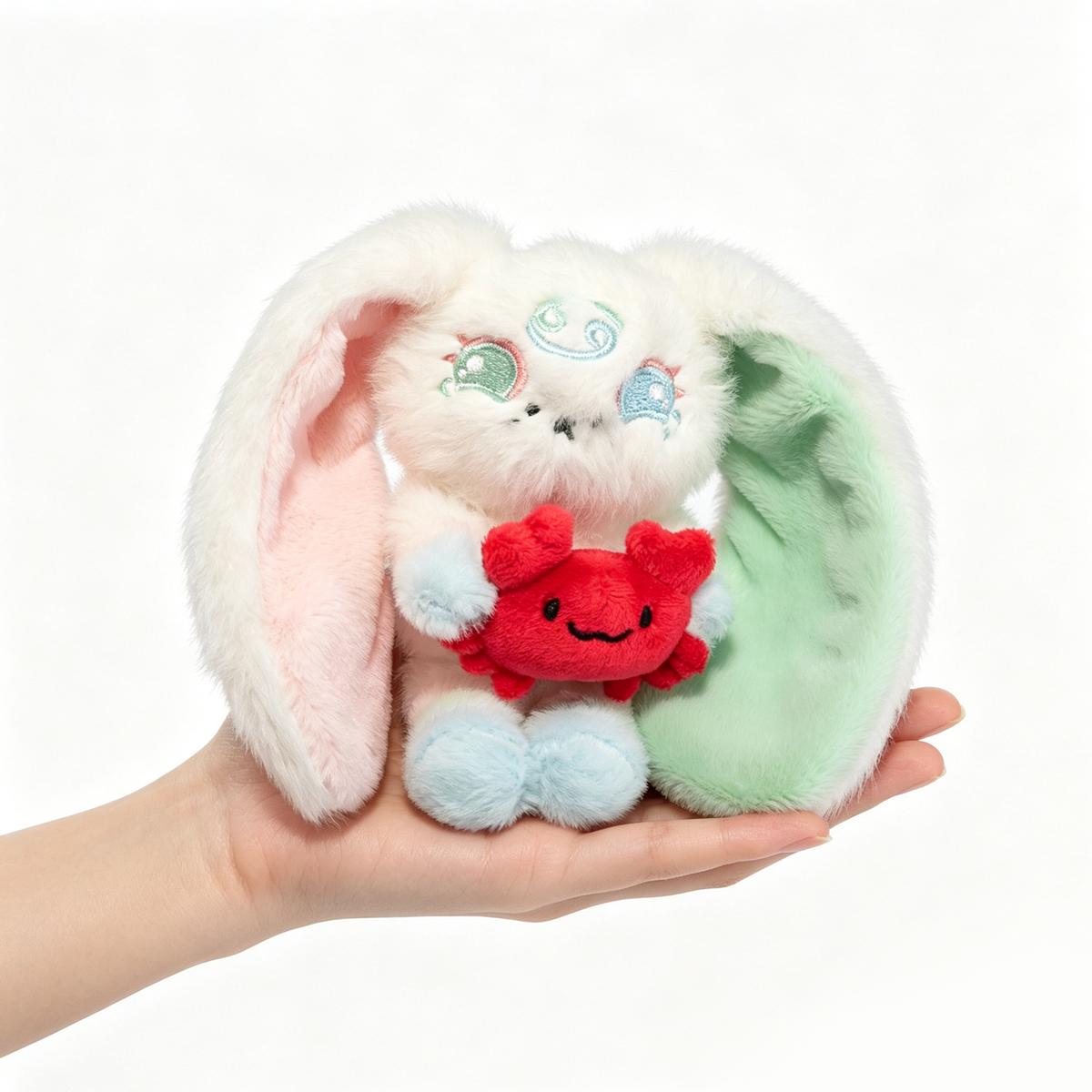 A Plushie Dreadfuls bunny with pastel ears hugs a red crab plush, perfect as a Cancer Zodiac Gift in your hand.