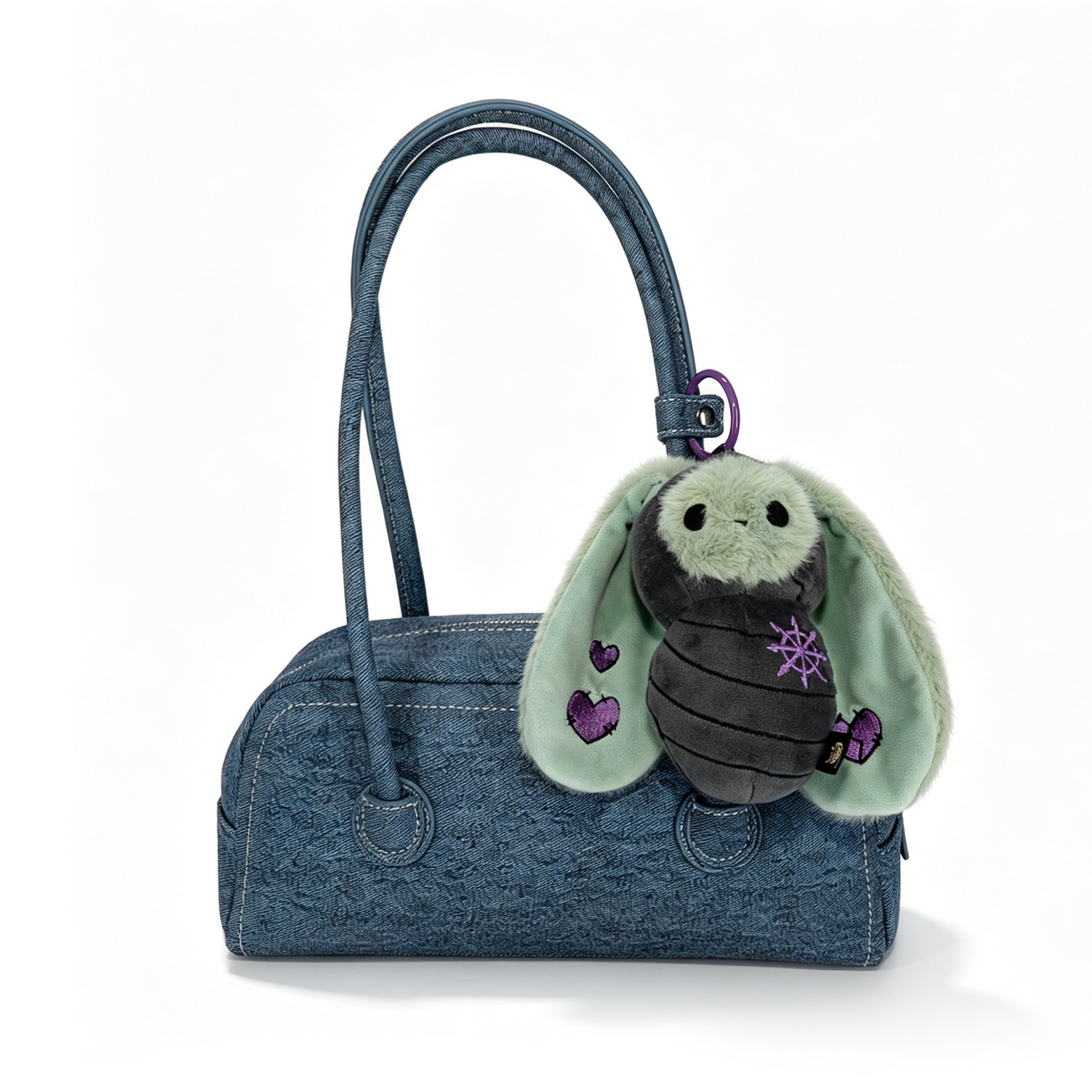 Blue handbag with a Bunnculus Plush Keychain, a green rabbit plush featuring purple hearts and star embroidery attached.