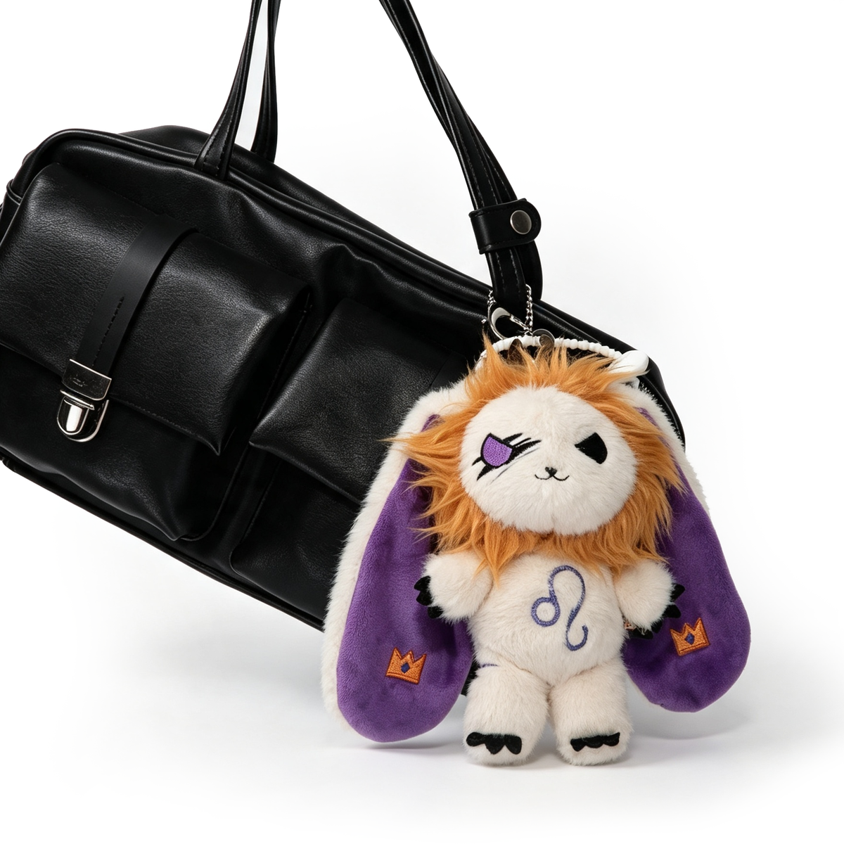 A Leo Plush Keychain with a lion mane and purple ears hangs from a black handbag by Plushie Dreadfuls.