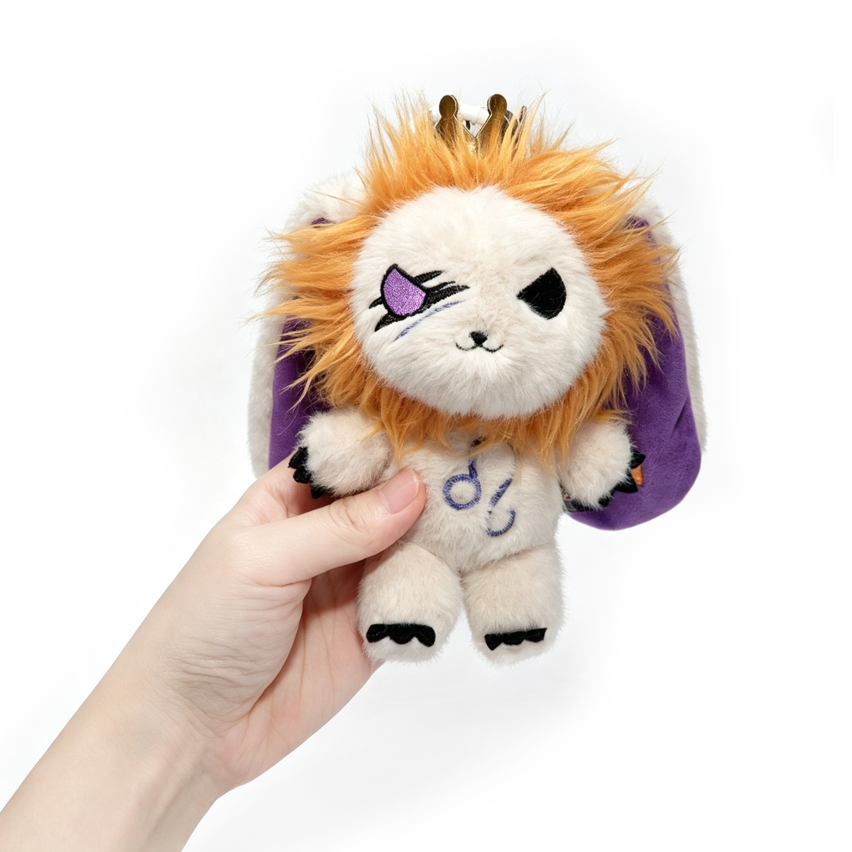 A hand holds the Leo Plush Keychain from Plushie Dreadfuls, featuring a crown, orange hair, and detailed stitching.