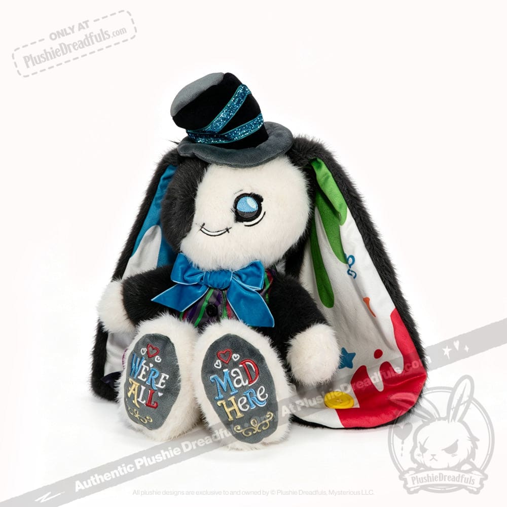A plushie rabbit in a hat and cape, with ADHD Mad Hatter vibes and Were All Mad Here embroidered on its feet.