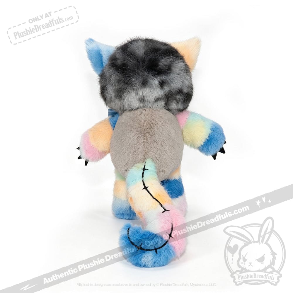 The Victorian McGee's Autism Acceptance Cheshire Cat - Plush Stuffed Animal is displayed upright against a white background, showcasing its gray back, pastel rainbow limbs and tail, black claws, furry ears, and distinctive black-stitched tail. Inspired by the whimsical world of Alice in Wonderland, this plush celebrates autism acceptance through its vibrant and inclusive colors.